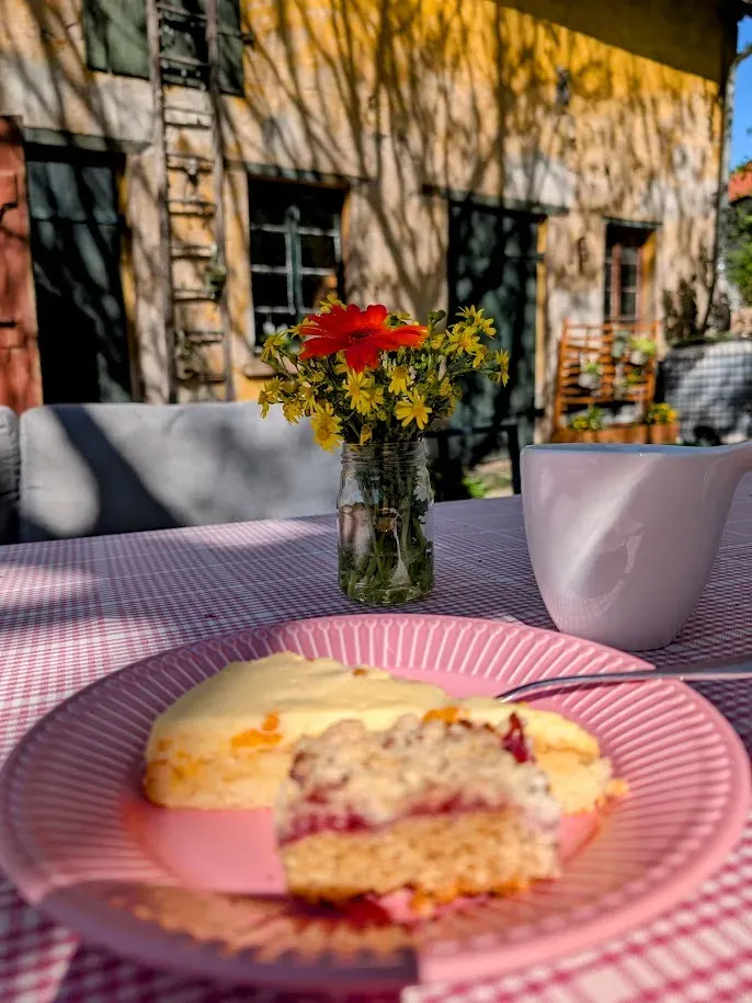 Kuchen und Wiesenblumen auf einem gedeckten Tisch im Hof vor dem Bauernhaus